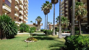 A hotel courtyard with palm trees, a lawn, and a building with multiple balconies. - Quiet Beachfront Oasis : Doña Sofía (Fuengirola)