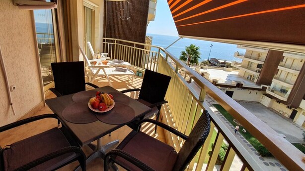 A balcony with a table set for two, a view of the sea, and a building complex in the background. - Quiet Beachfront Oasis : Doña Sofía (Fuengirola)