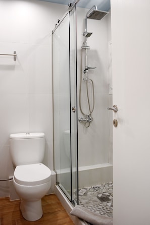 A bathroom with a toilet, a glass-enclosed shower with a handheld showerhead, and a tiled floor. - Armonia Deluxe Apt Must (Thessaloniki)