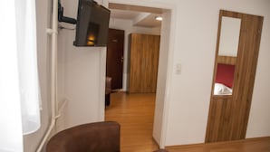 A hallway with a wooden floor, a brown chair, a wooden wardrobe, and a TV mounted on the wall. - Gästehaus Häuser (Linden)