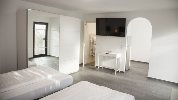 A modern bedroom with a bed, a desk, a TV, and a wardrobe. - Gästehaus Häuser (Linden)