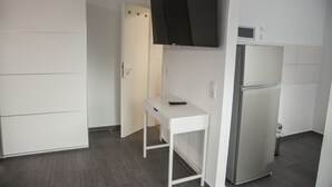 A compact kitchen with a white cabinet, a built-in microwave, a stainless steel refrigerator, and a white table with a remote control on it. - Gästehaus Häuser (Linden)