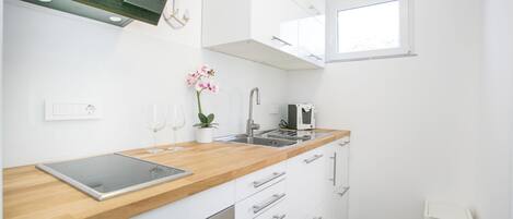 A modern kitchen with white cabinets, a wooden countertop, a built-in oven, a sink, and a window.
