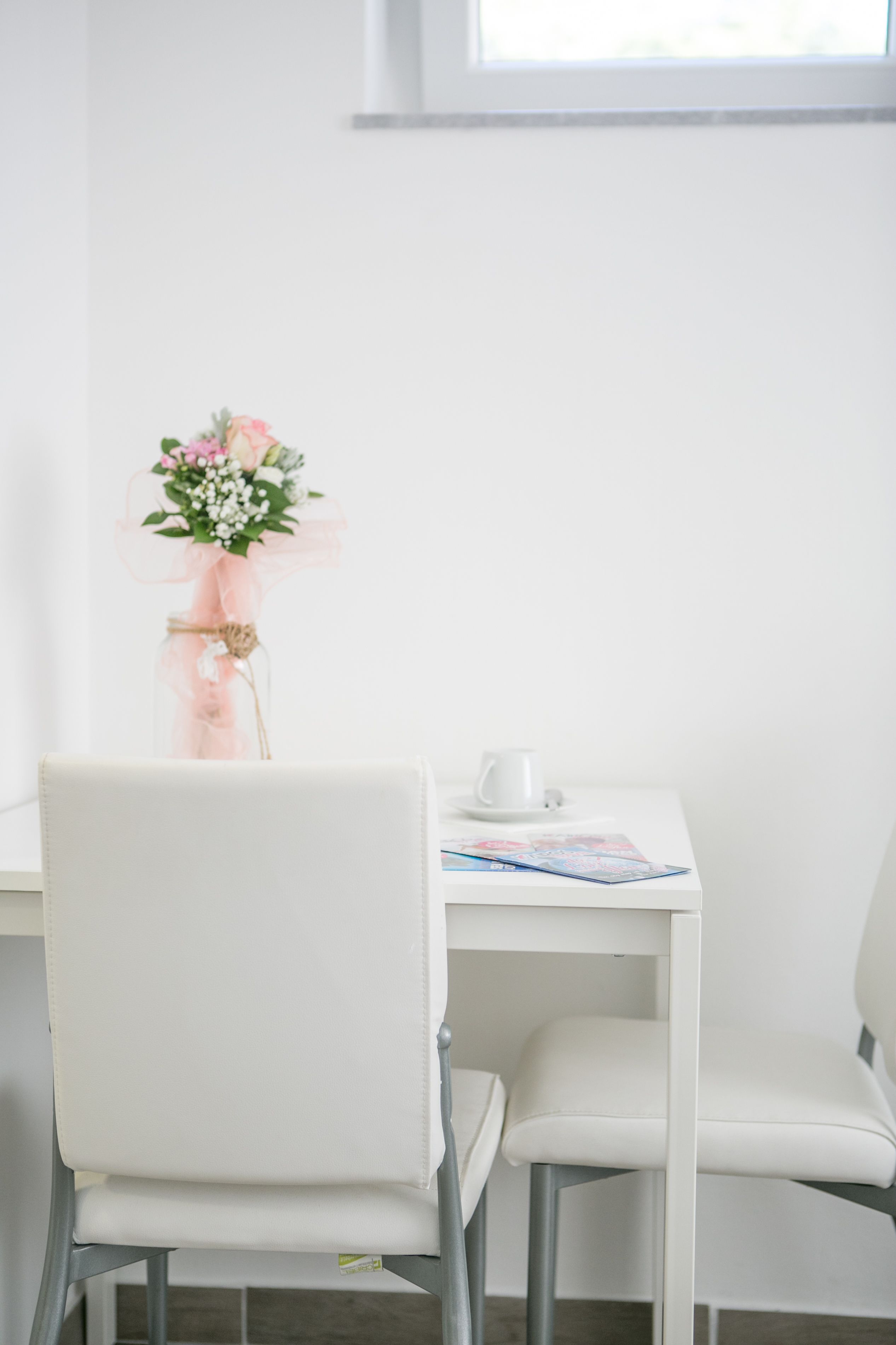 Una sedia e un tavolo con un piccolo bouquet di fiori e una tazza bianca.