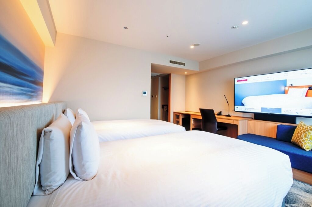 A hotel room with two beds, a desk, a television, and a sofa.