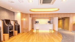 Una hall d'albergo moderna con pavimento in legno, una reception e un'area giochi con cabinati arcade.