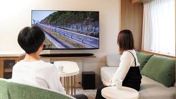 A room with a television displaying a scenic landscape, a sofa, a small table, and a window with curtains.