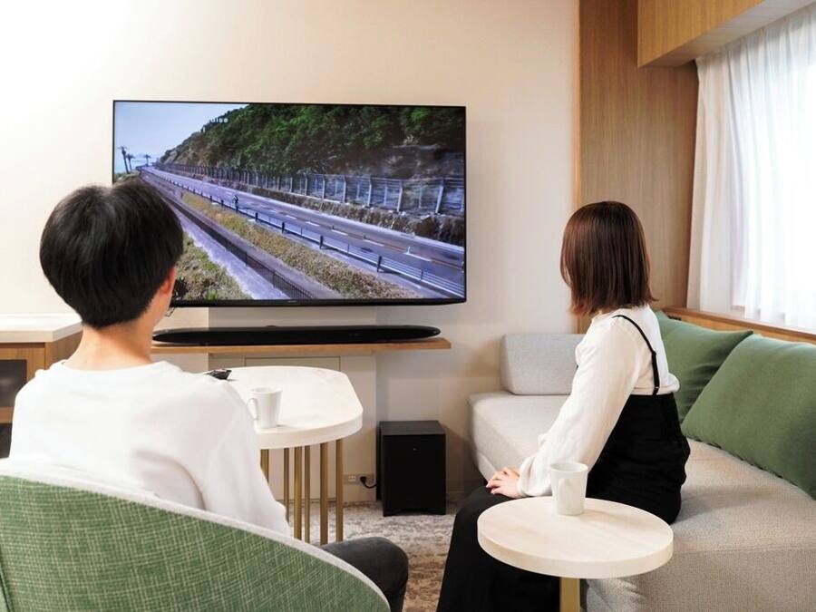 A room with a television displaying a scenic landscape, a sofa, a small table, and a window with curtains.