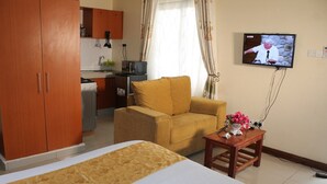 A hotel room with a bed, a sofa, a small table with a vase, and a television on the wall.
