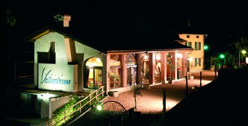 Um hotel com entrada bem iluminada, placa visível e área ajardinada com um caminho que leva à entrada.