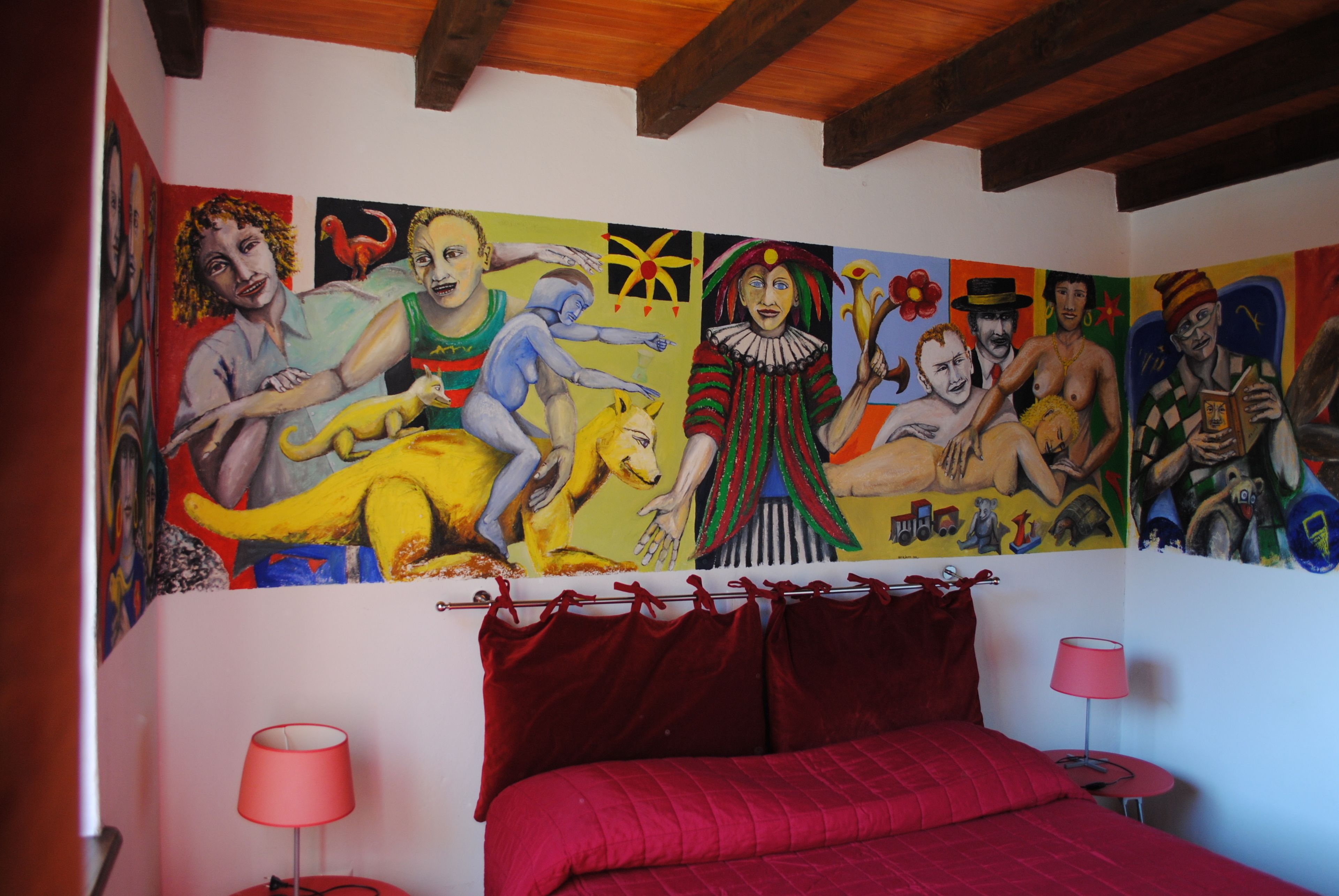 Ein Schlafzimmer mit einer großen Wandmalerei, einer roten Bettdecke und zwei Nachttischlampen.
