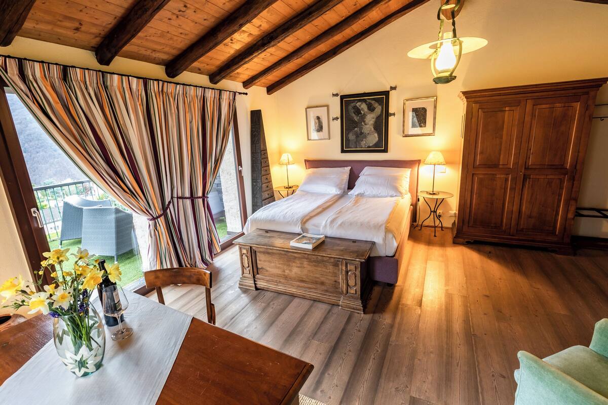 A bedroom with a wooden bed, bedside lamps, a wooden cabinet, and a view of the outdoors.
