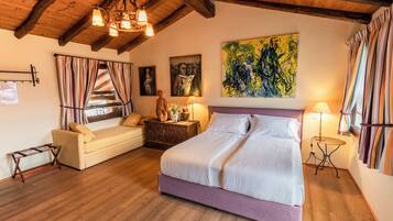 A bedroom with a bed, a sofa, a wooden floor, a chandelier, and artwork on the walls.