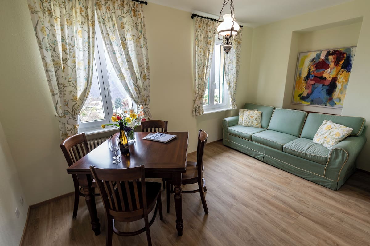 A dining area with a wooden table and chairs, a green sofa, and floral curtains.