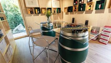 A bar area with a glass counter, metal chairs, and a large green barrel. Shelves with bottles and a menu board are visible.