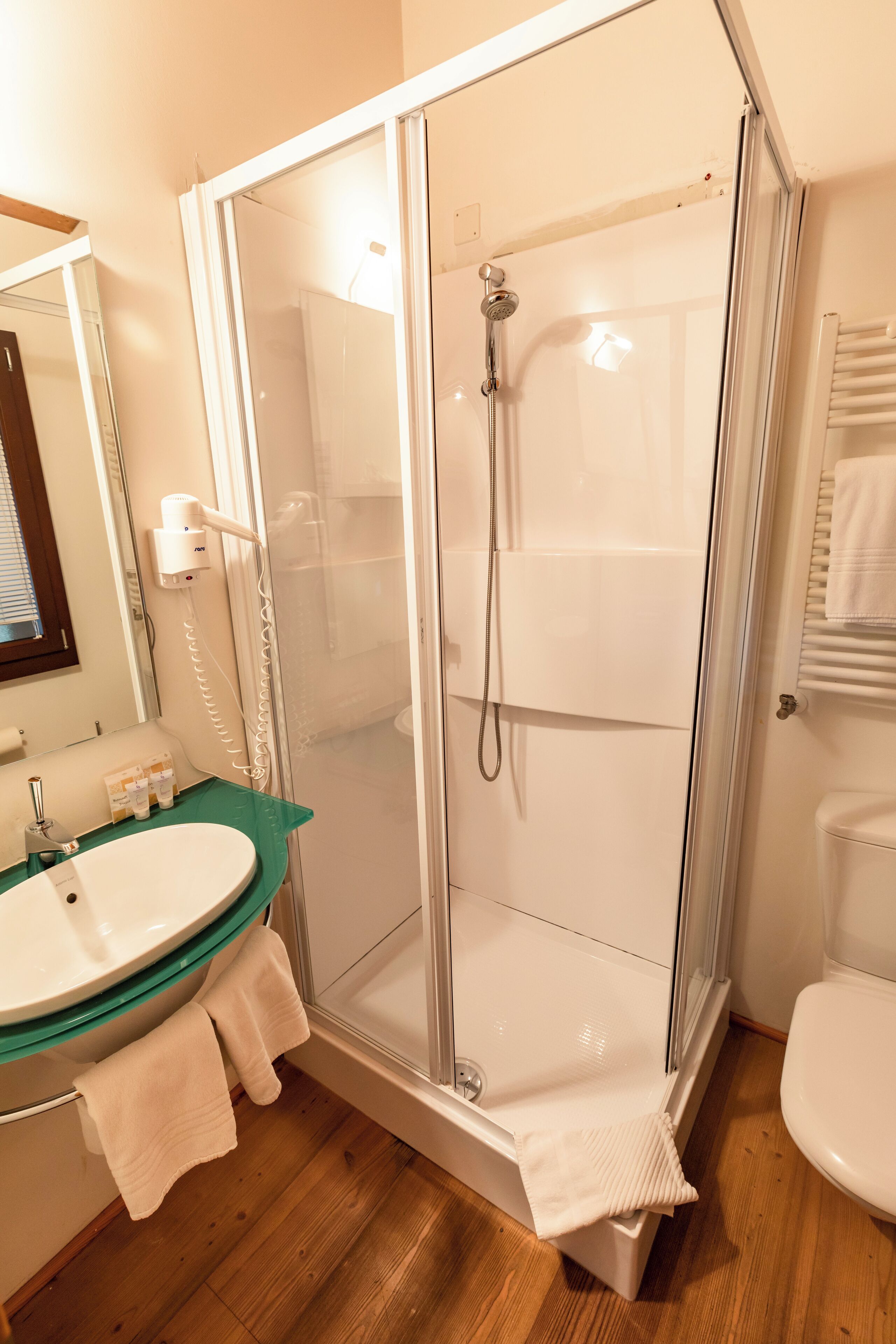 Un baño con cabina de ducha de vidrio, lavabo con encimera verde y retrete blanco.