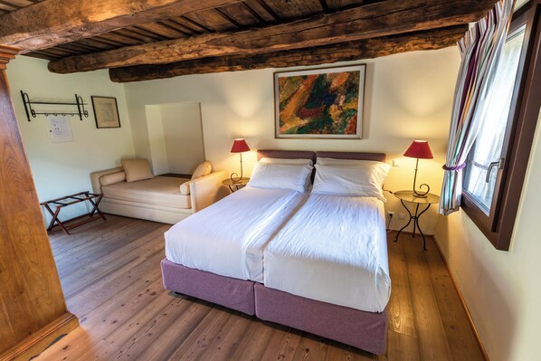 A bedroom with a large bed, two bedside tables with lamps, a sofa, and a wooden ceiling.