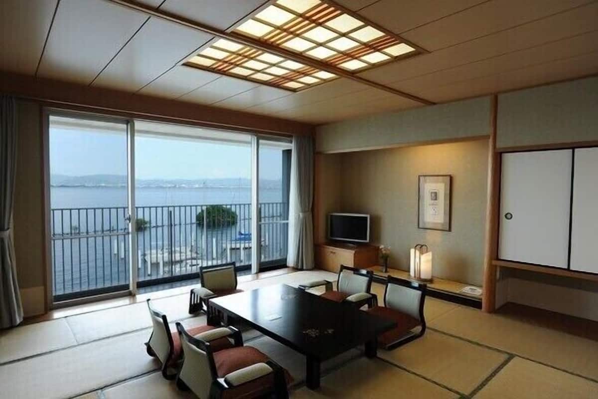 A hotel room with a large sliding glass door to a balcony, a flat-screen TV, a dining table with chairs, and a traditional Japanese-style cabinet.