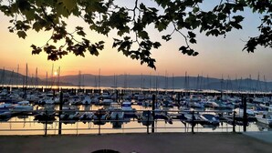 Satamassa on useita laivoja, vesi on tyyni ja taivaalla näkyy auringonlasku.