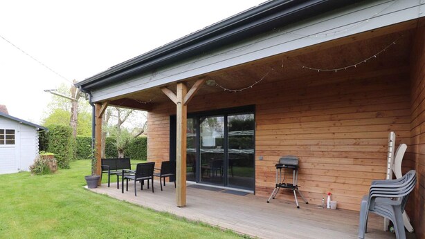 Une terrasse en bois avec des meubles d’extérieur, un patio couvert et une porte-fenêtre coulissante donnant sur un jardin.