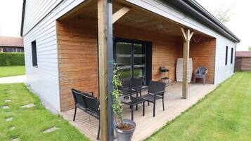 A covered patio with a wooden deck, outdoor seating, and a potted plant.