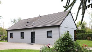 Une maison de plain-pied à l’extérieur gris, avec un toit foncé et un petit porche à l’avant.
