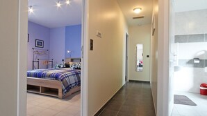 Un couloir étroit mène à une chambre à coucher équipée d’un lit et à une salle de bain avec douche.