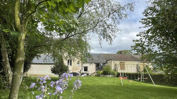 Une maison avec une pelouse bien entretenue, une balançoire et un jardin où poussent des fleurs violettes.