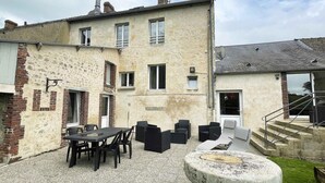 Un bâtiment à deux étages doté d’un patio comprenant une table et des chaises, un banc en pierre et un petit jardin.