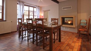 Une salle à manger avec une table et des chaises en bois, une cheminée et une fenêtre avec des rideaux.
