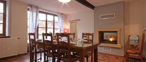 A dining area with a fireplace, wooden chairs, a table set for four, and a window with curtains.