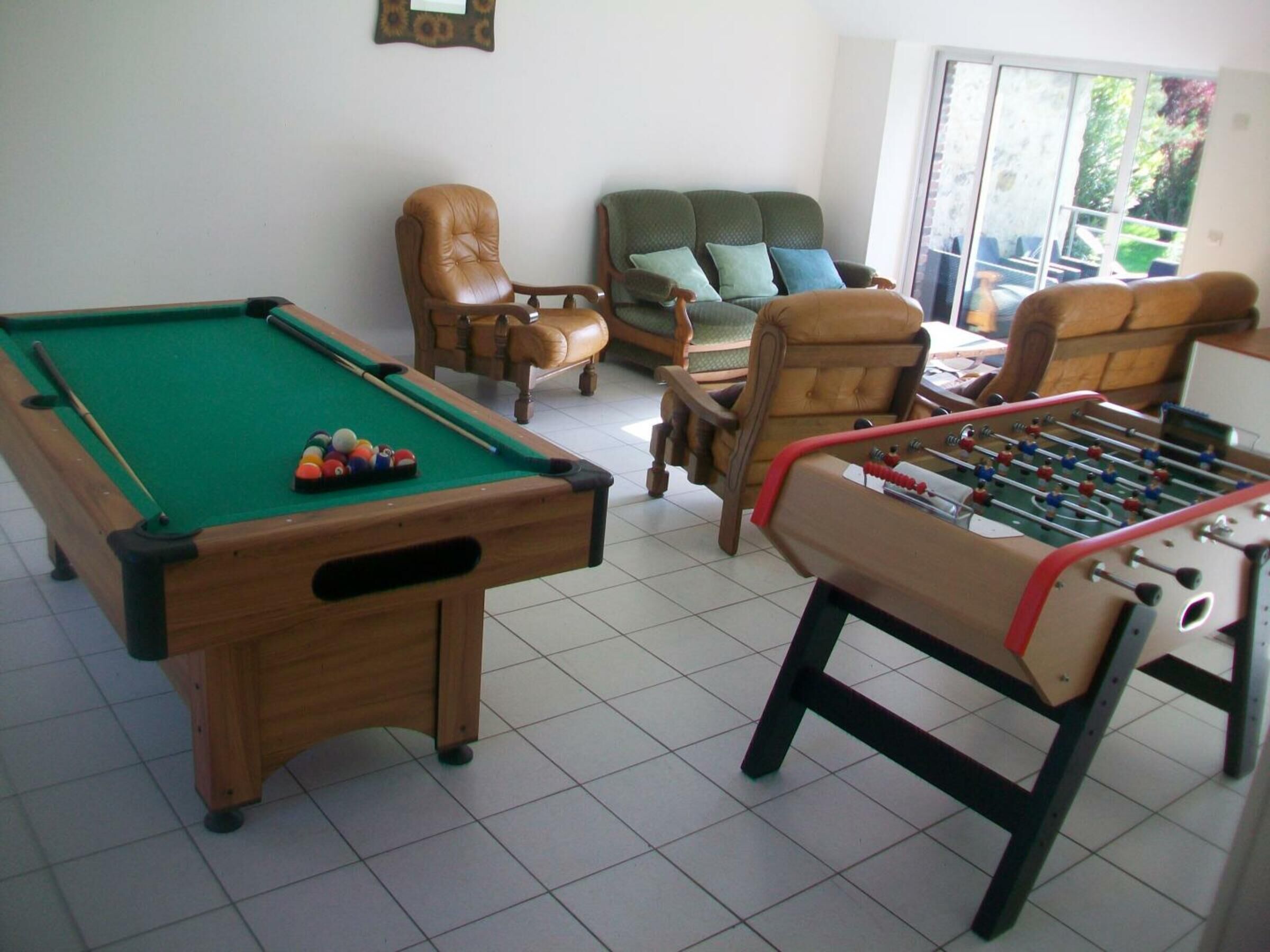 A room with a pool table, a foosball table, and two armchairs.