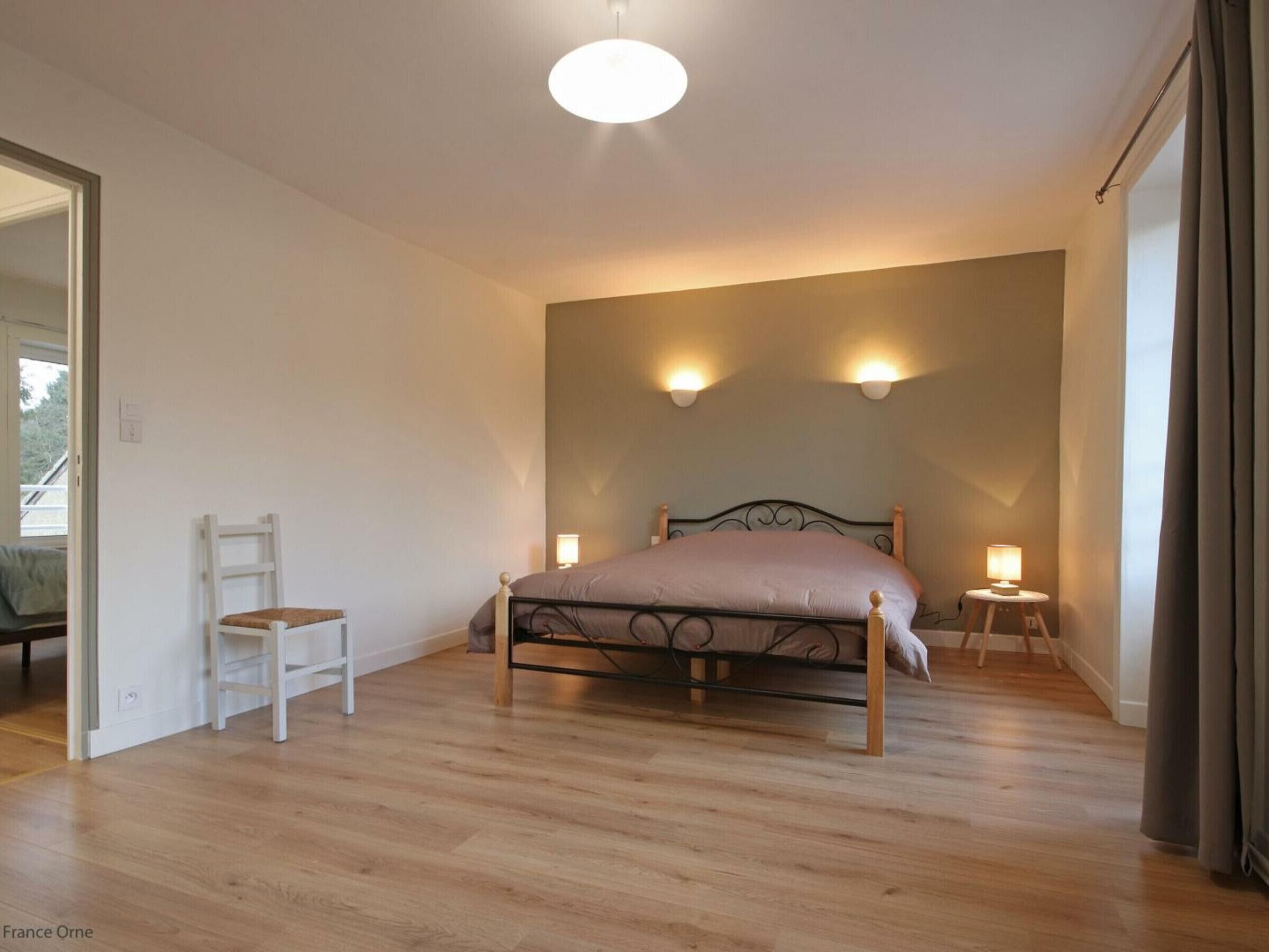 A bedroom with a bed, a chair, two bedside lamps, and a large window with curtains.