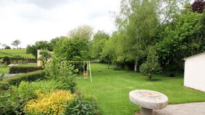 Un jardin bien entretenu, agrémenté d’une balançoire, d’un banc en pierre et de diverses plantes à fleurs.