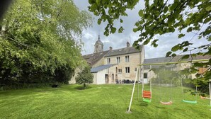 Une cour arrière verdoyante avec une balançoire et un bâtiment en pierre surmonté d’une tour, visible au loin.