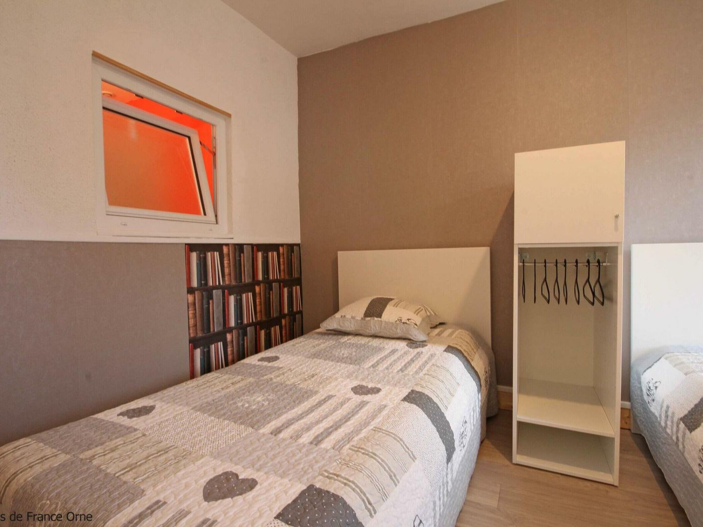 A bedroom with a bed, a bookshelf, a wardrobe, and a window with orange light.