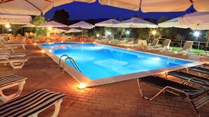 A swimming pool with lounge chairs and umbrellas, surrounded by brick flooring and night lighting. - Agriturismo Il Borgo sul Lago (Maierato)