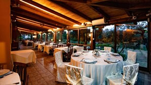 A restaurant with round tables covered in white tablecloths, wooden chairs, and a view of trees through large windows. - Agriturismo Il Borgo sul Lago (Maierato)