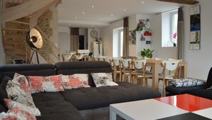 Una sala de estar moderna con un sofá oscuro, un comedor con sillas de madera, una escalera y un ventanal grande.