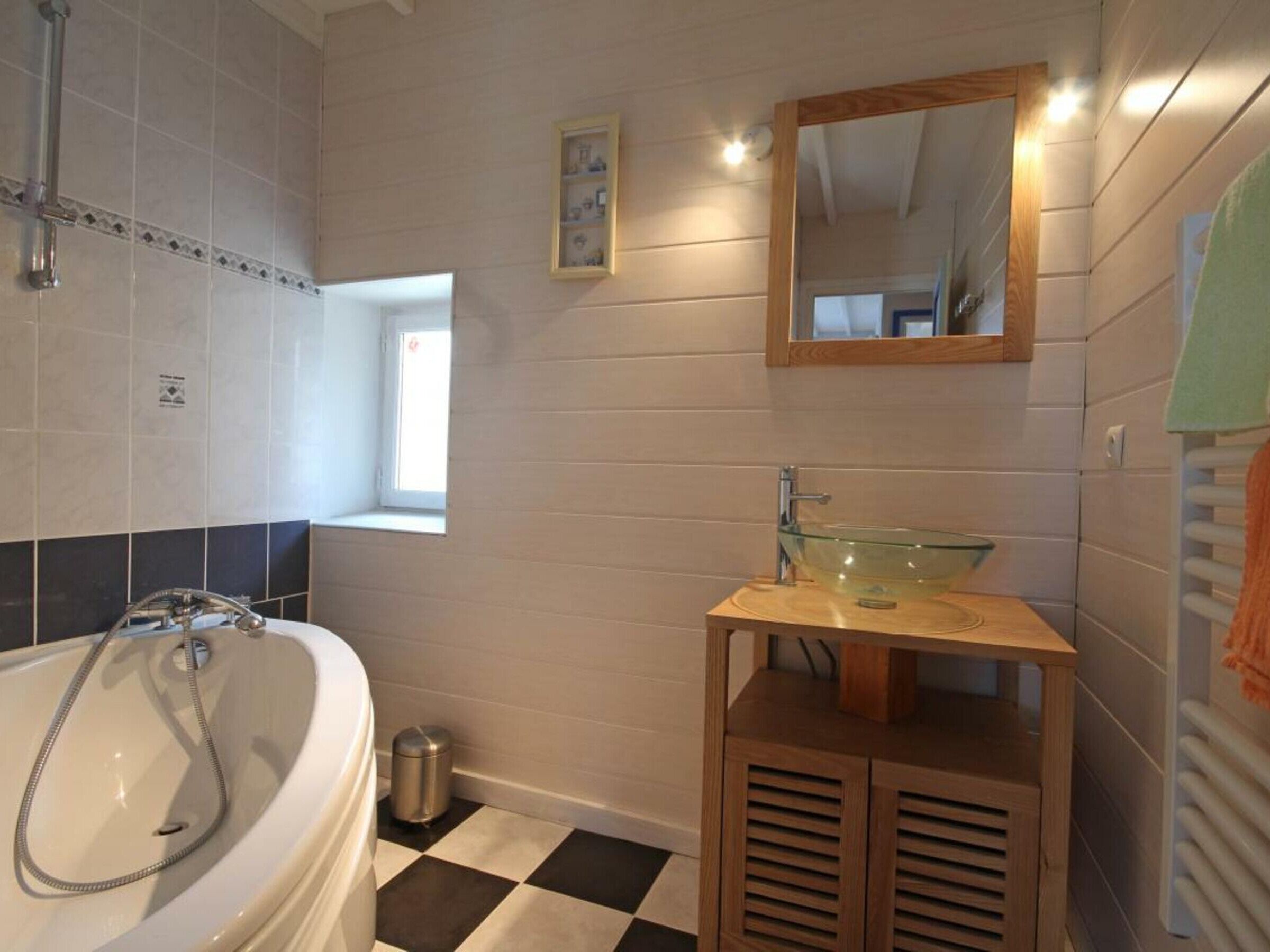 A bathroom with a bathtub, a glass sink on a wooden pedestal, a window, and a mirror on the wall.