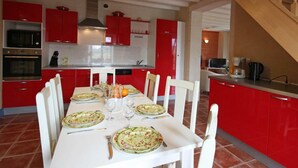 A modern kitchen with red cabinets, white chairs, and a dining table set for four. - Family house in the heart of Perche - 11 guests (Feings)