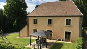 A two-story house with a patio area featuring a table and chairs under a canopy. - Family house in the heart of Perche - 11 guests (Feings)