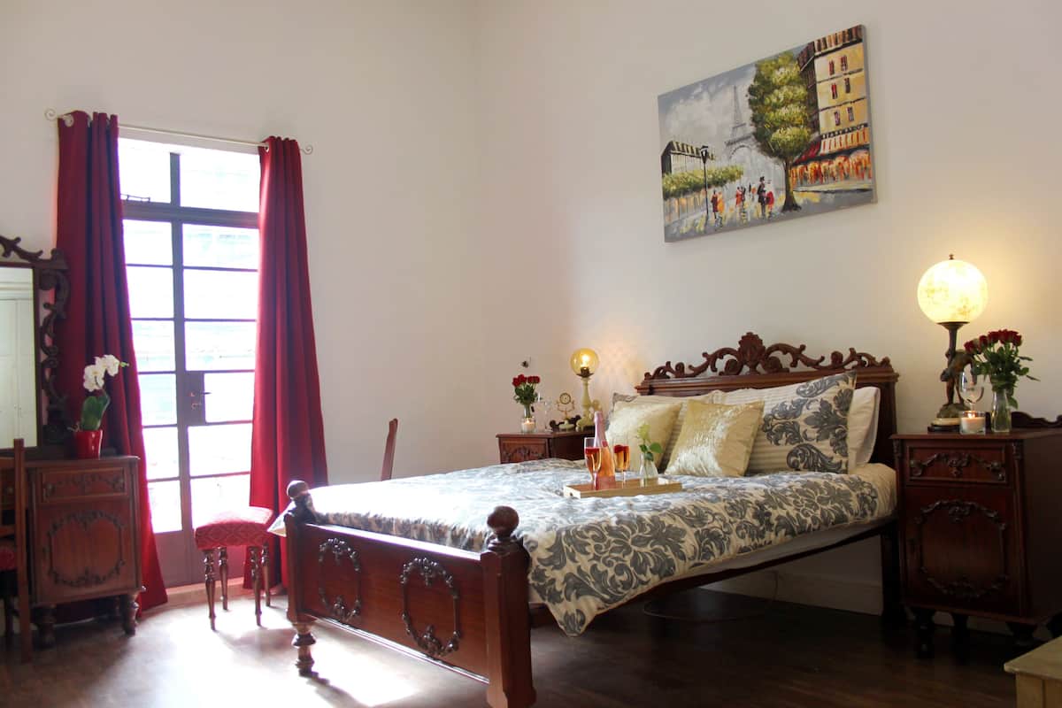 Un dormitorio con una cama grande, muebles de madera, un cuadro de París y una ventana con cortinas rojas.