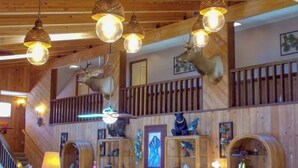 Un interior rústico con vigas de madera, un balcón con barandilla y diversas trofeos de animales exhibidos en estanterías.