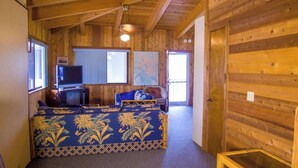Interior de una cabaña de madera con cama, televisor y ventana.