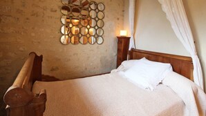 Ein Schlafzimmer mit einem hölzernen Bett, einem wandmontierten Spiegel, einem Nachttisch mit Lampe und einem Baldachinbett.