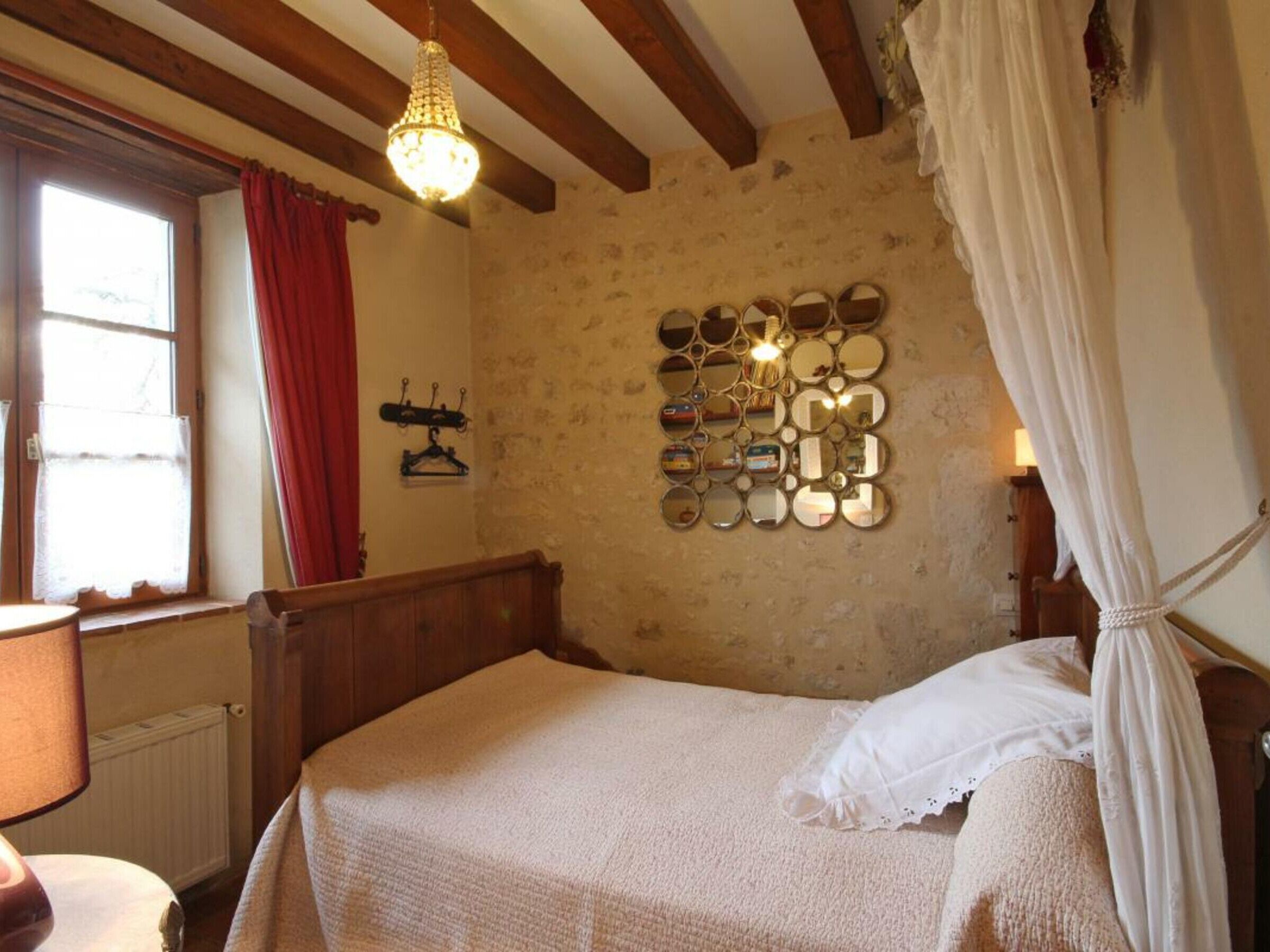 Une chambre à coucher comprenant un lit, un miroir décoratif fixé au mur, une fenêtre avec des rideaux et un lustre.