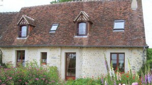 Ein zweistöckiges Steinhaus mit einem geneigten Dach, Dachfenstern und einem Garten mit verschiedenen Blumen.
