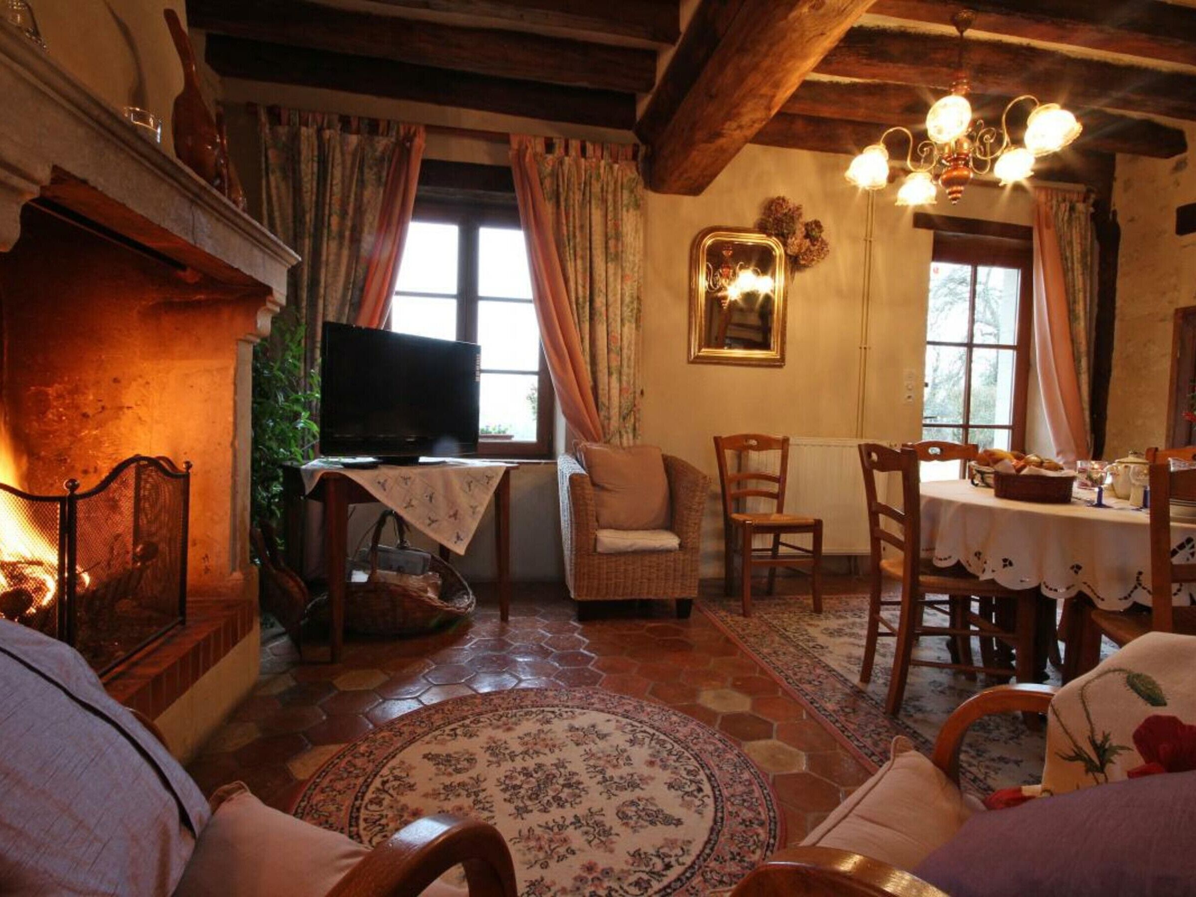 Un salon chaleureux avec une cheminée, un téléviseur et un coin repas où une table est dressée pour deux personnes.
