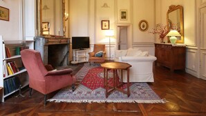A traditional living room with a fireplace, a television, a sofa, a red armchair, and a patterned rug.